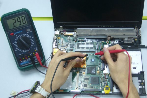 A technician testing components on a laptop motherboard